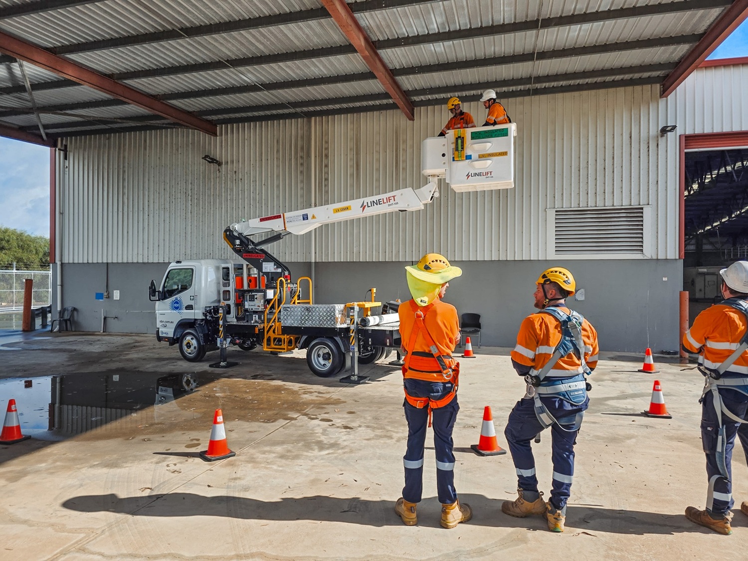 The Turnkey Truck Build Process Smarter EWP Solutions for Australian Businesses (2) Powerline workers look on as a white Linelift EWP bucket truck is demonstrated to them with the boom and bucket extended in their workyard.