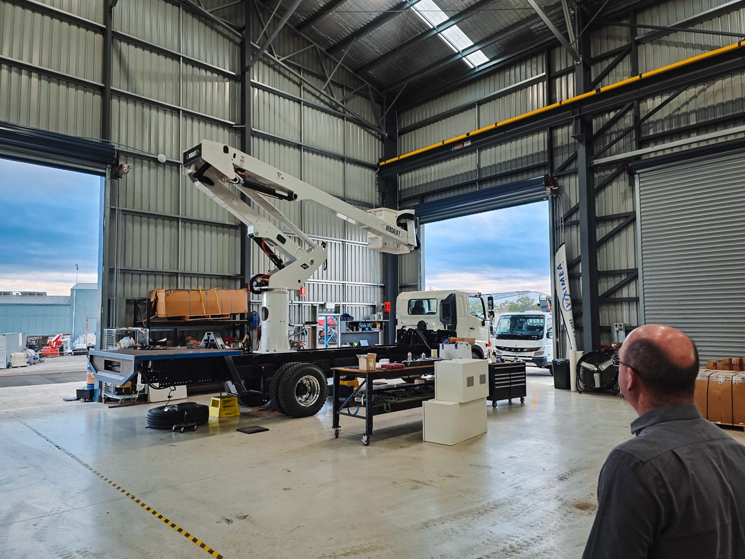 The Turnkey Truck Build Process Smarter EWP Solutions for Australian Businesses (3) Powerline workers look on as a white Linelift EWP bucket truck is demonstrated to them with the boom and bucket extended in their workyard.