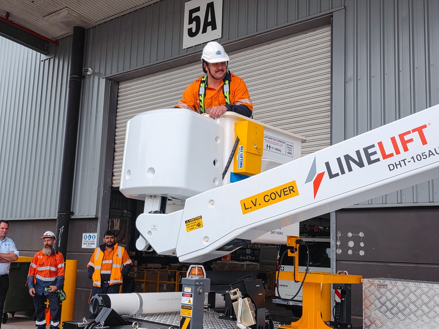 The Turnkey Truck Build Process Smarter EWP Solutions for Australian Businesses (5) Powerline workers look on as a white Linelift EWP bucket truck is demonstrated to them with the boom and bucket extended in their workyard.